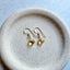 Pair of gold earrings with citrine gemstones on a beige plate against a light blue background