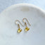 Gold earrings with yellow citrine gemstones on a white plate
