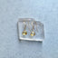 Gold earrings with yellow citrine gemstones on a clear crystal block against a light blue background