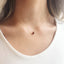 Gold necklace with a red garnet gemstone worn by a person on a white background