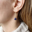 Close-up of an ear wearing a blue sapphire teardrop earring with gold chain.
