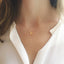 Gold necklace with a small citrine pendant worn by a person in a white shirt.