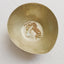Gold opal birthstone necklace with a pendant in a brass bowl on a textured white surface