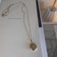 Gold filled round locket necklace on delicate chain displayed on book page with minimalist styling