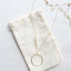 Long circle opal necklace with minimalist gold pendant on a soft fabric background