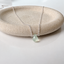 Prehnite teardrop necklace in sterling silver on a stone dish