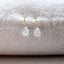     Dainty pear shaped moonstone earrings displayed on neutral textured fabric with delicate gold filled ear wires