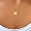 Close-up of a gold-filled initial disc with opal teardrop worn on the neck, October birthstone