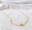Tiny faceted peridot bead necklace on a gold filled cable chain resting on white linen