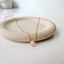 Gold filled pink opal teardrop necklace draped over a stone dish