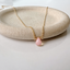 Pink opal teardrop pendant on a gold chain resting on a textured dish