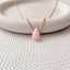 Faceted Peruvian pink opal teardrop on a gold filled chain over a stone dish