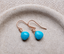 Turquoise dangle earrings in rose gold filled with faceted heart-shaped turquoise briolettes on ear wires, in a speckled ceramic dish