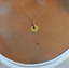 Close-up of a gold-filled initial disc with ruby teardrop worn on the neck