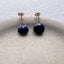 Close-up of blue sapphire stud earrings with gold settings displayed on a neutral jewelry stand.