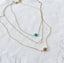 A collection of Gold necklaces with a single turquoise, moonstone, and labradorite necklaces on a white linen fabric background