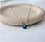Sterling silver London blue topaz teardrop necklace with faceted briolette on a speckled stone dish