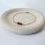 Three faceted tiger's eye beads on a 14k gold-filled bracelet on a speckled ceramic dish