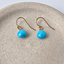 Gold filled turquoise dangle earrings with bright blue faceted briolettes in a speckled ceramic dish