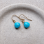 Gold filled turquoise dangle earrings on a speckled ceramic dish beside woven linen