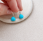 Turquoise dangle earrings in sterling silver with faceted turquoise briolettes held over a stone on cream linen