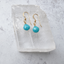 Gold filled turquoise dangle earrings resting on a clear crystal slab