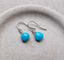 Turquoise dangle earrings in sterling silver with faceted heart-shaped turquoise briolettes on ear wires, in a speckled ceramic dish