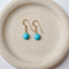Turquoise dangle earrings in 14k gold filled with faceted heart-shaped turquoise briolettes on ear wires, in a speckled ceramic dish