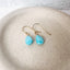 Handmade turquoise drop earrings displayed on a neutral beige jewelry dish