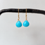 Turquoise dangle earrings hanging from a black rod, showing gold filled ear wires and faceted turquoise stones