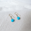 Turquoise dangle earrings in gold filled lying on white linen fabric