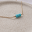 Gold-filled turquoise bar necklace with three faceted turquoise beads on a stone dish