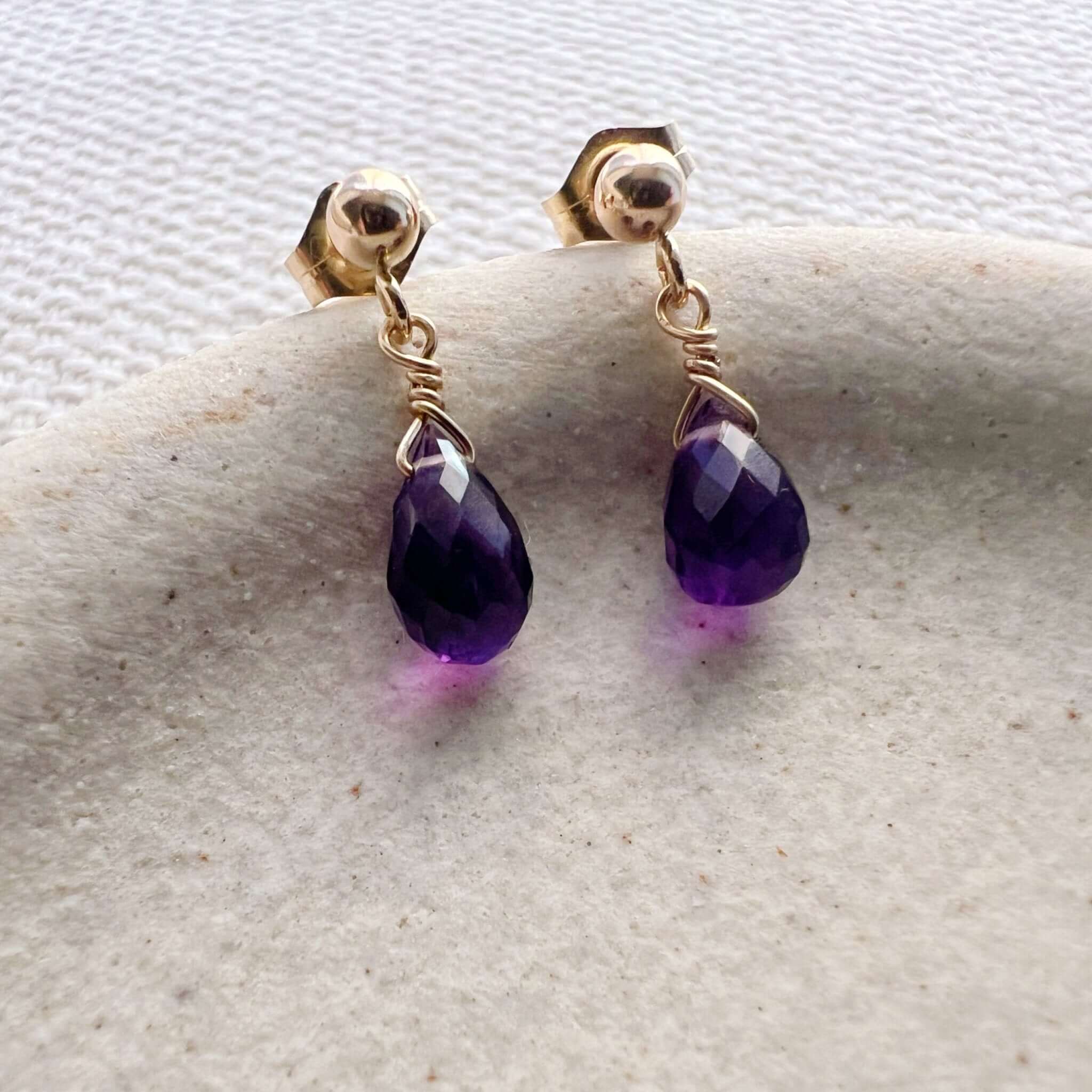 Dainty amethyst teardrop stud earrings displayed on a stoneware jewelry dish