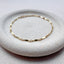 A dainty gold dapped chain bracelet displayed on a stoneware jewelry dish