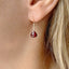 model is shown wearing a garnet birthstone earring that dangles from a simple gold ear wire
