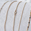 A collection of bracelets displayed on linen fabric showing a gold satellite chain bracelet, gold rolo chain bracelet, bezel set crystal gold rolo chain bracelet, gold curb chain bracelet and gold dapped chain bracelet