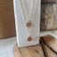 Two rose gold initial disc necklaces with K and E pendants displayed on a white textured stand with wood accents​​​​​​​​​​​​​​​​