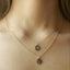 I Close-up of two layered gold initial disc necklaces on skin, with hand stamped M and L pendants