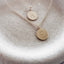 Two gold initial disc necklaces with K and E hand stamped pendants resting in a ceramic dish
