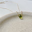 A dainty teardrop briolette peridot is displayed on a stoneware jewelry tray