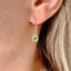 model is shown wearing a peridot birthstone earring that dangles from a simple gold ear wire