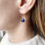 model is shown wearing a sapphire birthstone earring that dangles from a simple gold ear wire